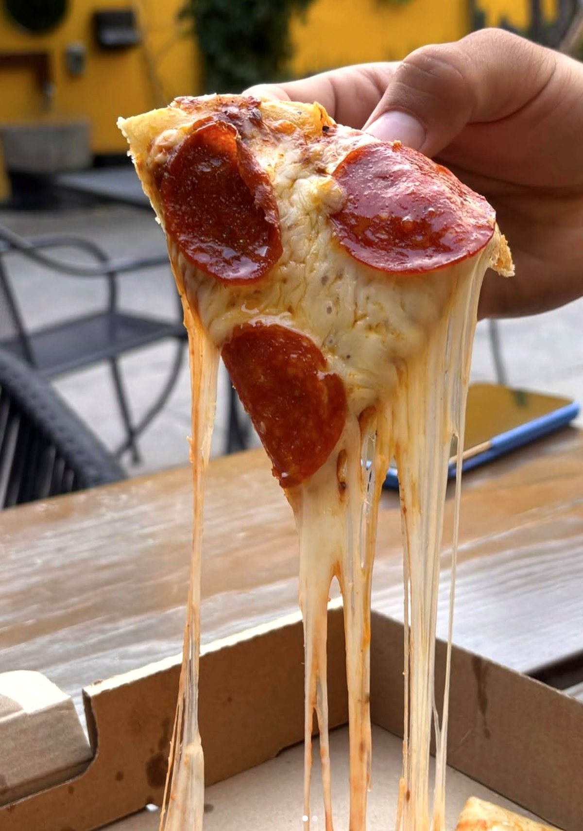 Rebanada de pizza de pepperoni con el queso estirándose, en el patio de Yahualica